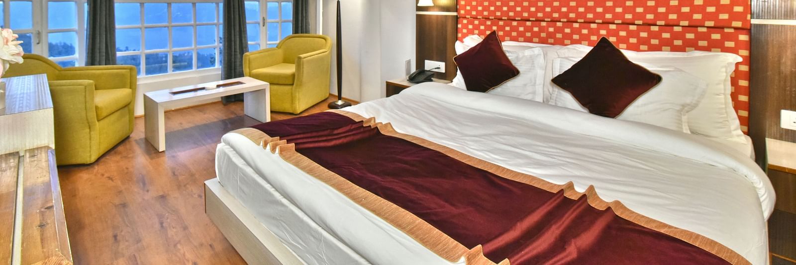 A bedroom with a seating area by the window, offering a mountain view at DLS Hillcrest Resort, Shimla.